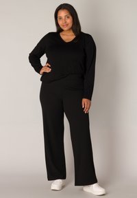 Zwarte lange mouwen top met een V-hals en losse broek set, beide gemaakt van zachte stof. Draagt met witte sneakers, wat zorgt voor een relaxte uitstraling.