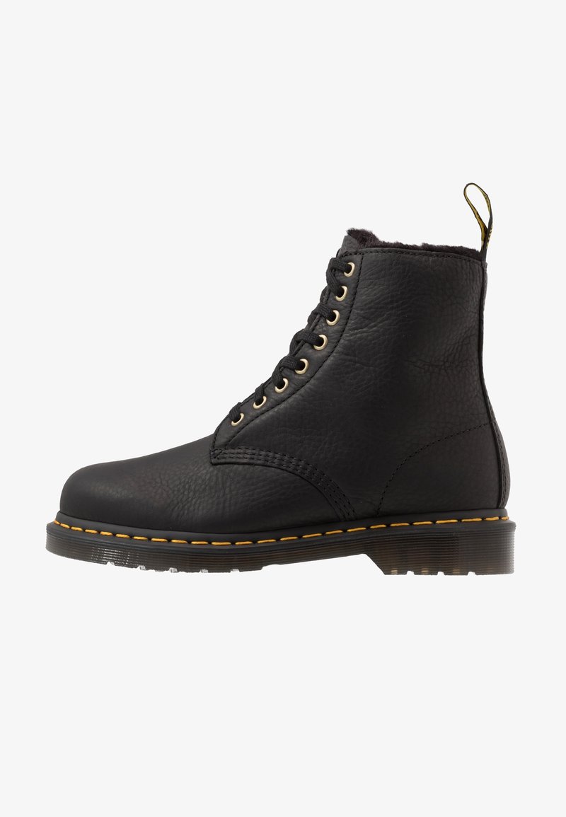 Bottine noire en cuir à lacets avec coutures jaunes, semelle épaisse en caoutchouc et languette au talon, vue de profil.