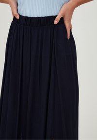 Mørk navy maxi nederdel med en ribbet elastisk talje, der har en let silhouette og sidelommer for funktionalitet. Blødt, tekstureret stof.