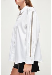 Camicia bianca con colletto, con maniche lunghe e una striscia grigia a contrasto lungo il lato. Tessuto morbido, vestibilità casual.