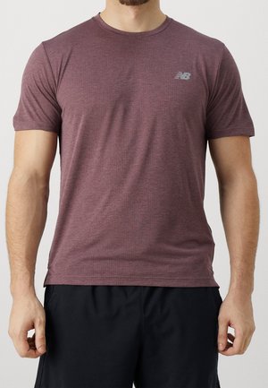 Man wearing a short-sleeve, maroon athletic t-shirt with a small New Balance logo on the left chest and black shorts.