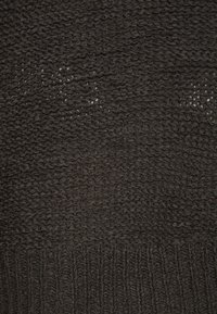 Dark knitted fabric with a textured pattern, featuring a mix of tight and loose stitches. The bottom section has a ribbed design.