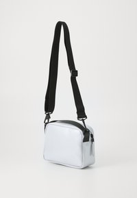 Sac bandoulière rectangulaire argenté avec une finition brillante, sangle noire réglable et anse supérieure noire. Comprend une fermeture éclair métallique et des détails en relief.