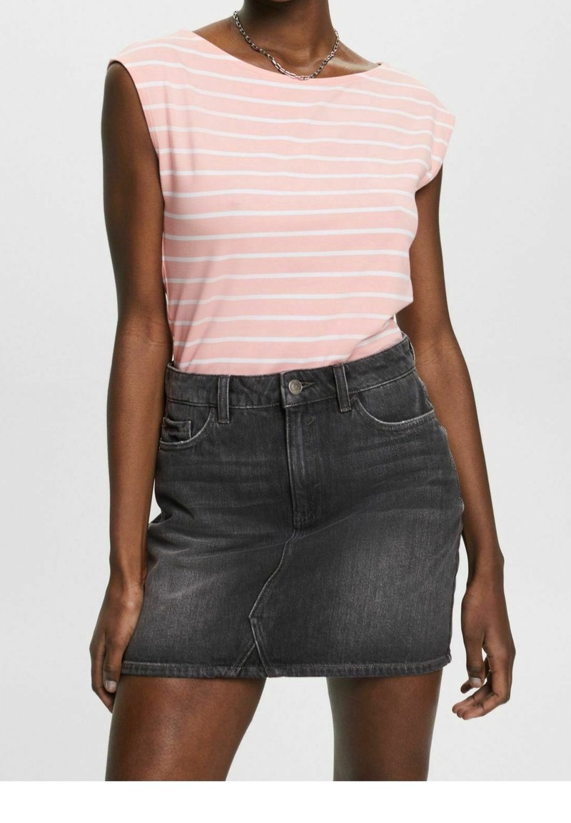 Femme portant un haut sans manches rayé rose et blanc, rentré dans une mini-jupe en jean noire délavée avec des poches avant.