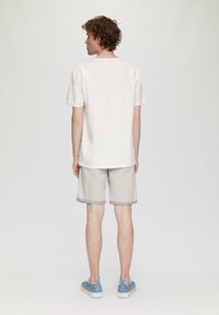 Lichtbeige t-shirt met korte mouwen, gecombineerd met lichtgrijze shorts. Schoenen hebben blauwe accenten en witte zolen. Minimalistisch ontwerp.