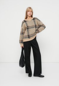 Beige en zwarte geblokte oversized trui van zachte brei, gecombineerd met zwarte wijde broek en een zwarte schoudertas.