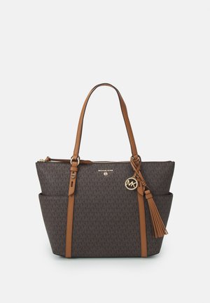 Bruine Michael Kors tote tas met gouden logo hanger, twee schouderbanden, zijzakken en een kwastdetail op een effen achtergrond.