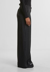 Pantaloni negri cu dungi subțiri, cu talie înaltă, având un design cu picioare largi și o textură de țesătură netedă. Accentuati cu buzunare laterale.