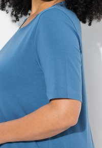 Modrá krátkosrstá košile s kulatým výstřihem, vyrobená z jemné, lehké tkaniny. Hladká textura a uvolněný střih.