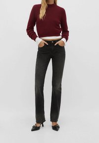 Black straight-leg jeans paired with a burgundy cropped sweater. The sweater features a ribbed neckline and long sleeves with white cuffs.