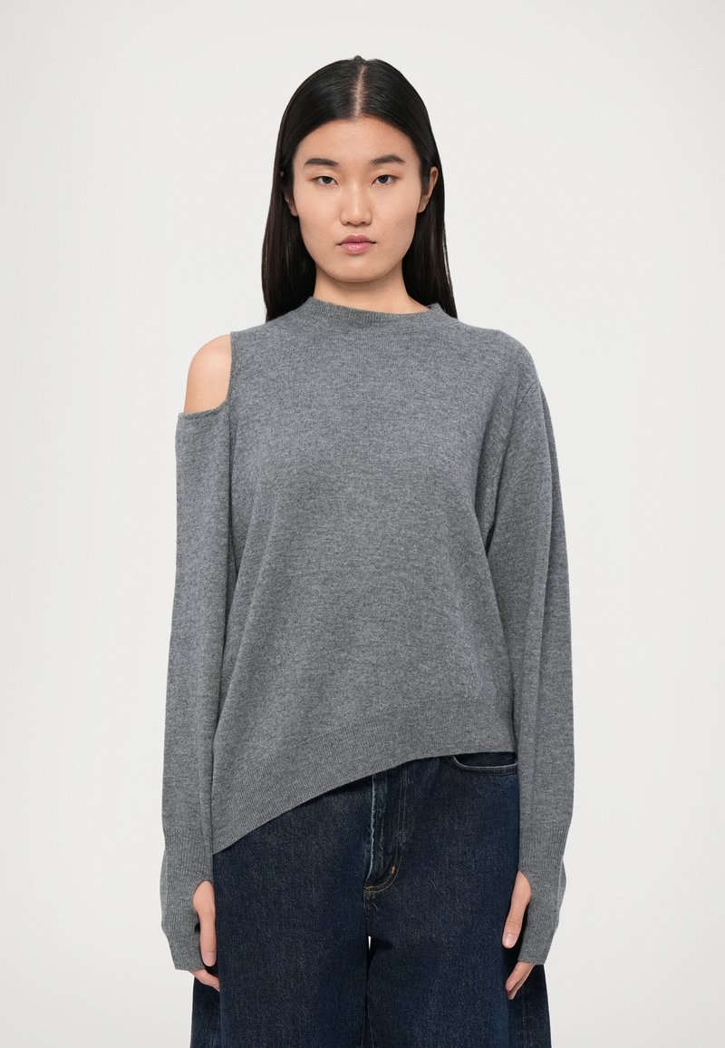 Maglione grigio a maglia con collo alto, maniche lunghe e dettaglio delle spalle scoperte. Texture morbida e vestibilità ampia, abbinato a jeans scuri.