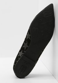 Zapato plano negro con punta, adornado con patrones de estrellas plateadas, suela grabada con el logo "Pretty Ballerinas" y pequeños iconos de zapatillas de ballet.