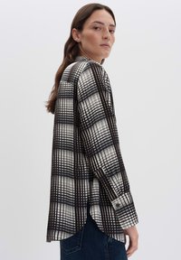 Camicia a quadri bianco e nero con maniche lunghe, caratterizzata da un polsino con bottone e un orlo curvato, realizzata in tessuto leggero.