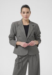 Šedý pruhovaný blazer s dlouhými rukávy, jednořadovým zapínáním a klopovými límci, doplněný volnými kalhotami ve stejném stylu.