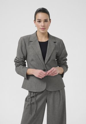Šedý pruhovaný blazer s dlouhými rukávy, jednořadovým zapínáním a klopovými límci, doplněný volnými kalhotami ve stejném stylu.