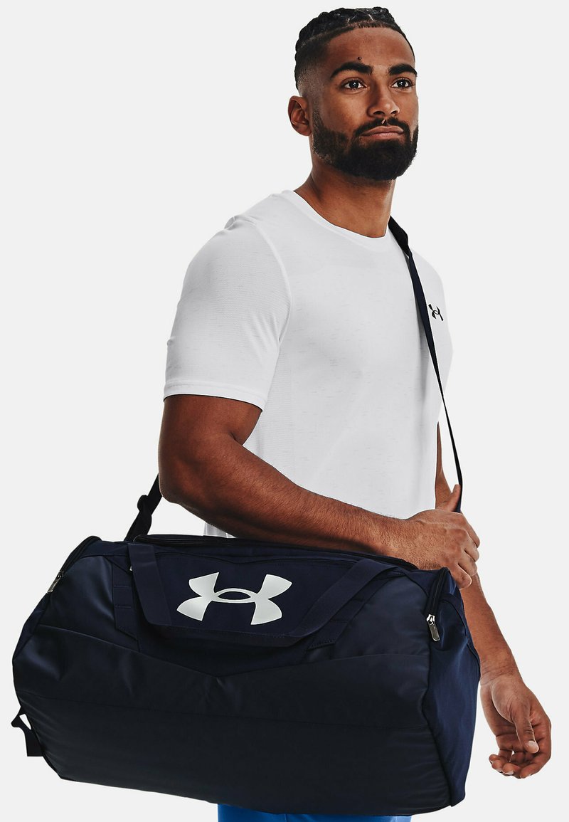 Laos duffel bag navy yang terbuat dari kain yang tahan lama, menampilkan logo putih besar, penutup ritsleting atas, dan tali bahu yang dapat disesuaikan.
