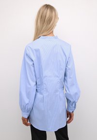 Ljusblå randig skjorta med avslappnad passform, knäppta manschetter och rundad nederkant. Baksidan har en mittsöm med detaljer. Slät tygtextur.