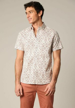Chemise à manches courtes avec boutons, de couleur blanche, ornée d'un motif floral rouge et bleu. Présente un col montant et une coupe décontractée.