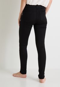 Jeans negros ajustados con cintura alta y bolsillos traseros, hechos de una tela suave, que muestran un diseño slim-fit.