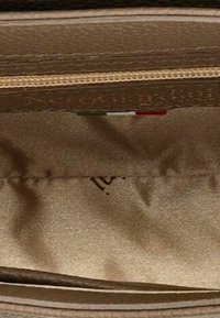 Intérieur en tissu beige avec des coutures, une fermeture éclair avec des dents beiges et une petite étiquette avec des rayures vertes, blanches et rouges.
