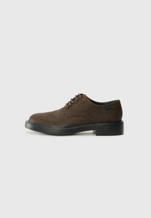 Brown suede lace-up shoe with a rounded toe, purple laces, and a black, slightly raised sole. Features stitched detailing on the sides.