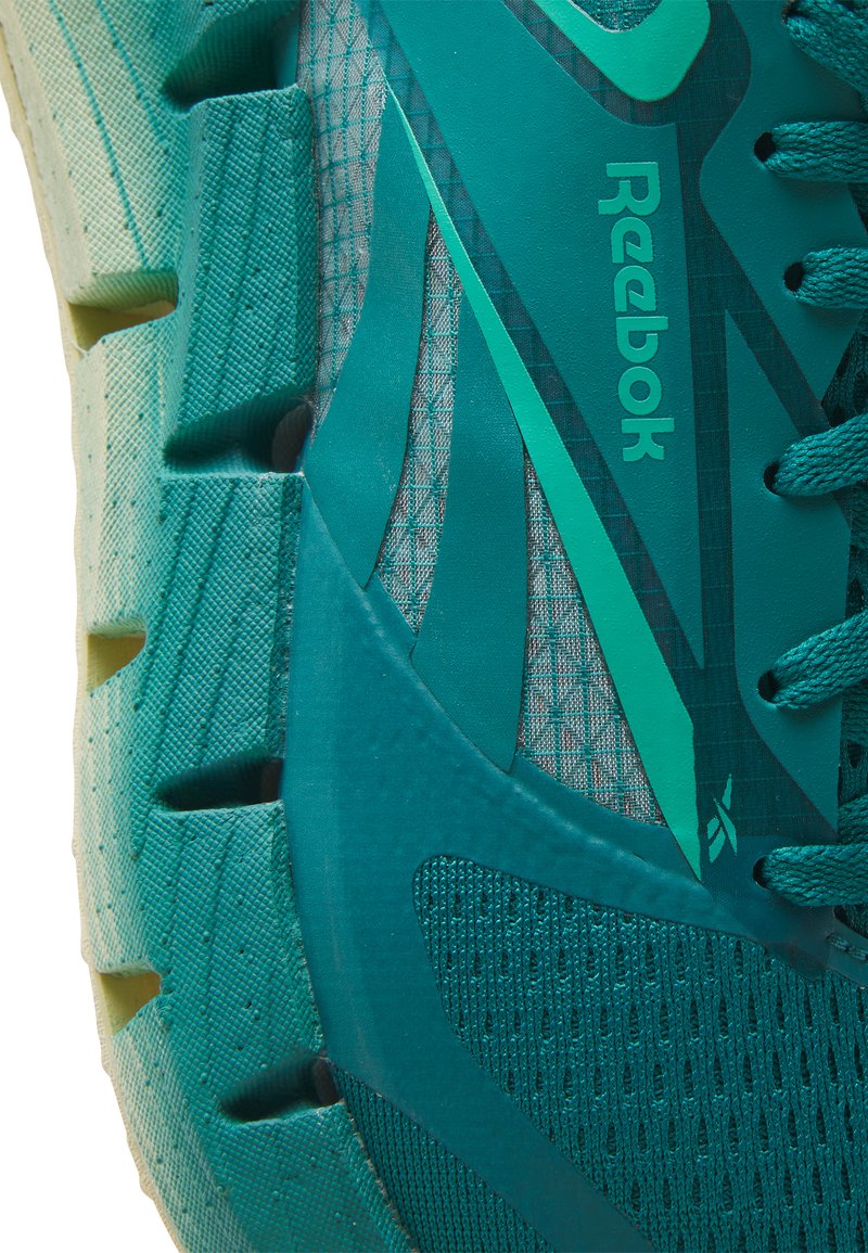 Zapatilla deportiva turquesa con una parte superior de malla texturizada, logotipo destacado de Reebok y suela de goma contorneada con profundas ranuras y recortes.