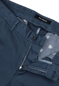 Marineblaue Hose aus glattem Stoff mit Knopf- und Reißverschluss, kontrastierender gemusterter Fütterung mit kleinen Formen. Markenlabel sichtbar.
