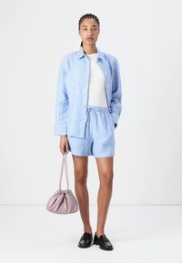 Chemise en lin bleu clair à rayures et shorts assortis, haut blanc en dessous, accompagné d'un sac rose et de mocassins noirs.