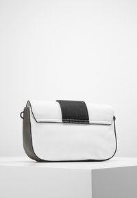 Bolso cruzado de cuero blanco y negro con forma rectangular, con una solapa texturizada negra y detalles de costura en contraste.