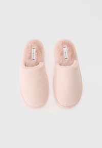 Kerge roosa plush slip-on susside paar, mille sisetallas ja välisküljel on Tommy Hilfiger logo, valge tausta peal.