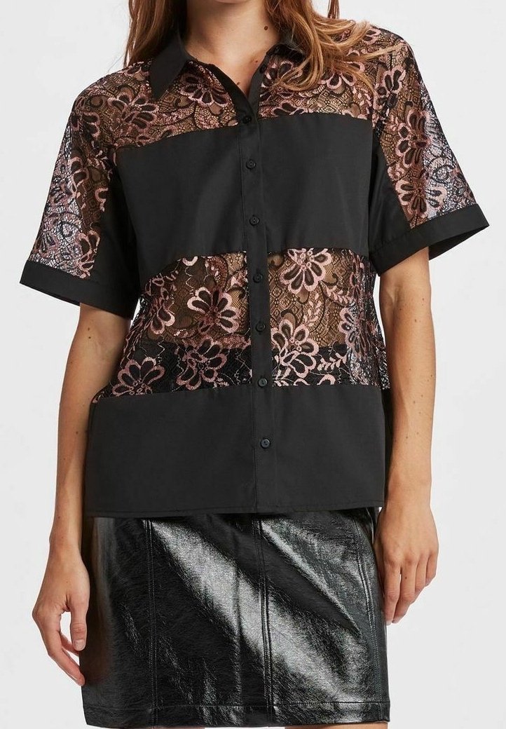 Femme portant une chemise à manches courtes avec des panneaux en tissu noir et des sections en dentelle florale, associée à une jupe en cuir noire brillante.