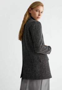 Blazer in tessuto nero e grigio con una vestibilità sartoriale, rever a punta e tasche laterali, caratterizzato da una spacco sul retro e maniche lunghe.