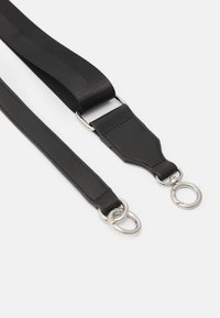 Due cinghie nere per borse con ganci metallici argentati su uno sfondo bianco: una cinghia in pelle, l'altra in tessuto intrecciato.