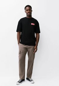 Must t-särk roosa "MARVEL" logoga, beež karupüksid taskutega ja mustad tossud valgete talladega. Lihtne, vabaaja riietus.