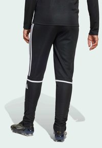 Czarne spodnie sportowe z białymi paskami po bokach, dopasowany krój, elastyczny materiał i ściągacze, w połączeniu z czarnymi korkami piłkarskimi.