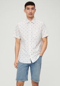 Camisa blanca de manga corta con pequeño patrón floral rojo, botones en la parte delantera, cuello y bolsillo en el pecho izquierdo, combinada con pantalones cortos de mezclilla.