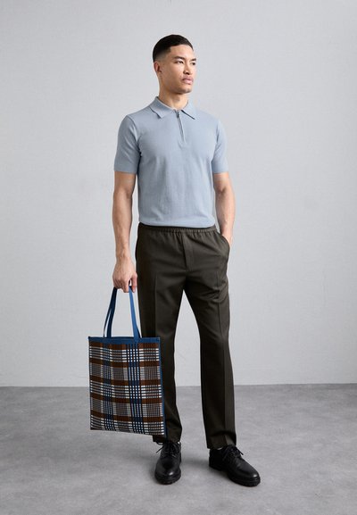 Polo shirt bleu clair à manches courtes avec un col, associé à un pantalon élastique taille haute vert foncé. Porte un sac fourre-tout à carreaux avec des poignées bleues.