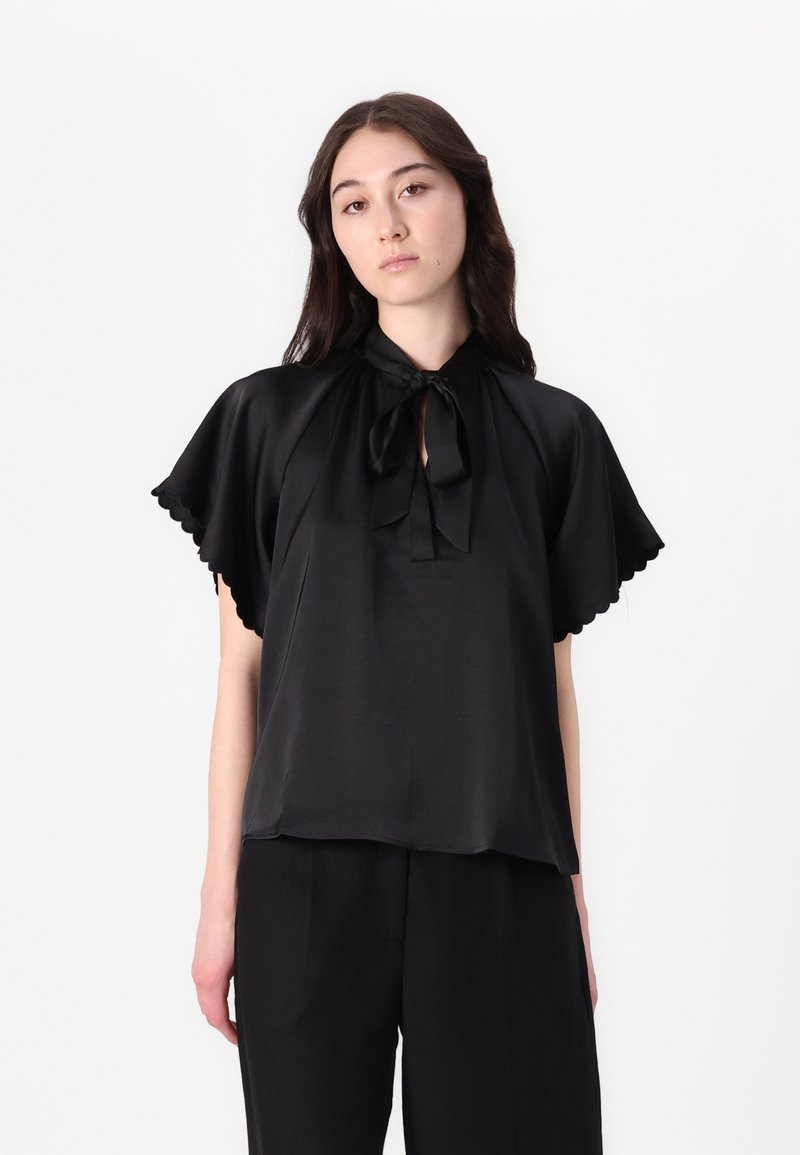 Blusa in satin nero con colletto legato e maniche scallop, caratterizzata da una vestibilità comoda e una leggera lucentezza su uno sfondo neutro.