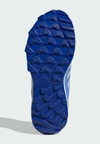 Modrá gumová podrážka s hlbokými, ostrými drážkami pre trakciu. Obsahuje hladký zaoblený opätok a textúrovaný povrch, označený výrazom "TRAXION."