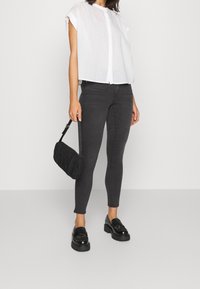 Witte korte mouwen overhemd met knopen, donkergrijze skinny jeans, zwarte gestructureerde handtas en zwarte instappers met dikke zolen.