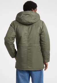 Olivgrüner Puffermantel mit Kapuze, ausgestattet mit einem Reißverschluss, elastischen Bündchen und einem Kordelzug in der Taille. Glatte, glänzende Außenfläche.