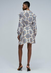 Vestido blanco con estampado floral en azul y naranja, mangas con volantes y cintura fruncida; combinado con tacones marrones; textura de tela suave.