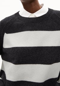 Neulottu neulepaita, jossa on tummanharmaat ja valkoiset vaakaraidat, pyöreä pääntie ja resorikuviointi kauluksessa ja olkapäillä.