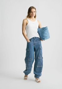 Valge tank top, millel on kõrgendatud logo, koos siniste täppidega cargo pükstega, kus on mitu taskut, ja kootud sinise kotiga. Valged kontsad.