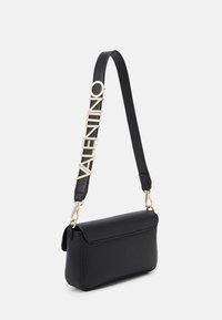 Černá kožená křížová taška s překlapávací klopou a zlatým logem "VALENTINO" na popruhu. Má strukturovaný materiál a elegantní tvar.