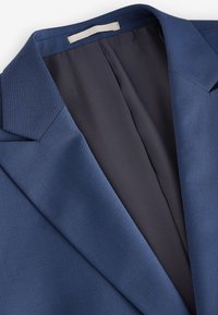 Blazer bleu cintré avec col à cran et doublure intérieure sombre, présenté à plat avec col visible et panneaux avant supérieurs.