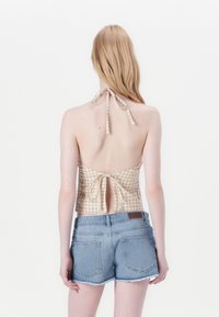 Top halter de cuadros vichy en beige y blanco con la espalda descubierta, atado al cuello y a la cintura, combinado con shorts de mezclilla claros.