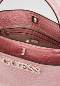 Borsa a tracolla rosa con logo dorato in rilievo, dotata di due tasche interiori e foderata in tessuto liscio. Chiusura superiore con dettaglio a chiusura magnetica.
