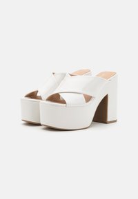 Mule in pattina bianca con plataforma, design a striscia incrociata larga, punta scoperta e tacco a blocco alto. Texture liscia con solette beige chiaro.
