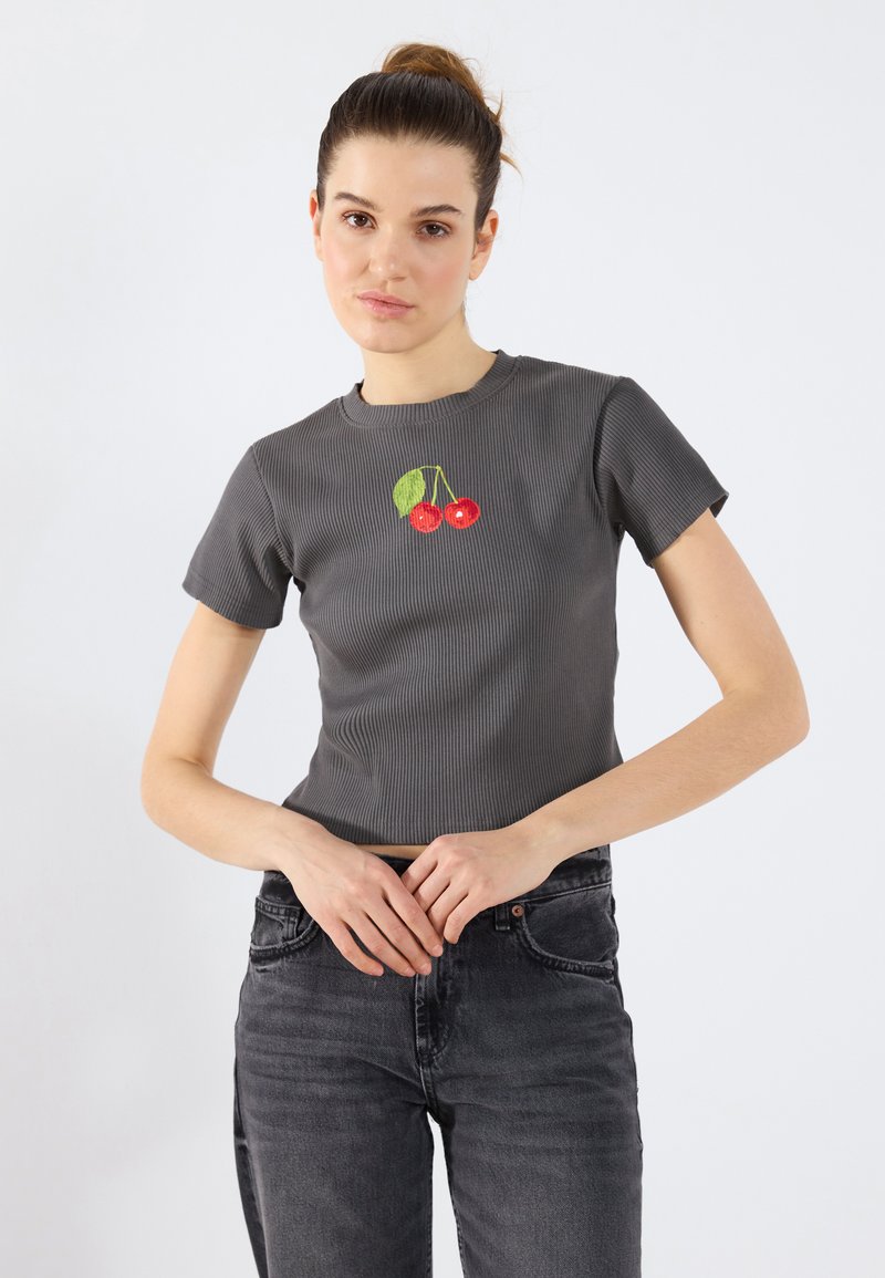 Grå stripete t-skjorte med kort erme som har et brodert kirsebærdesign i rødt og grønt i midten. Brukt med mørk grå jeans.